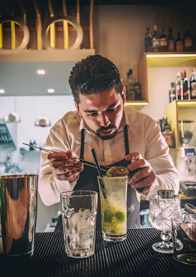 Barista meticulously garnishing a fresh kiwi mocktail with tweezers.